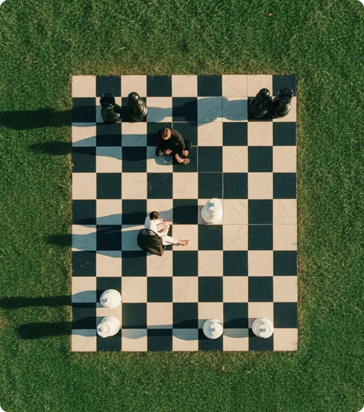 A giant chessboard laid out on a lawn, seen from above, with people standing among the pieces.