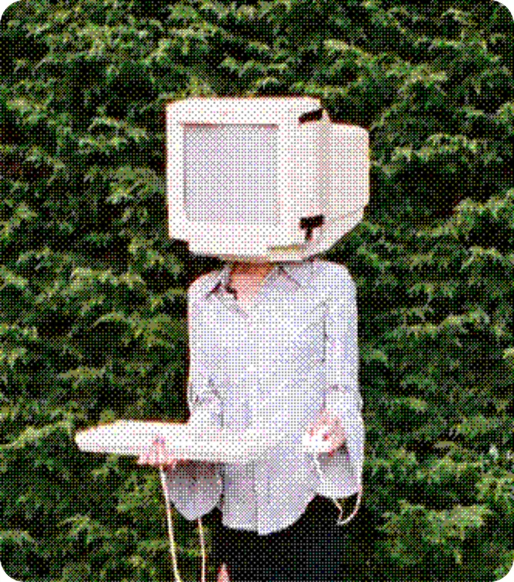 A person in a pale shirt stands against a dark hedge with a cardboard television box over their head.